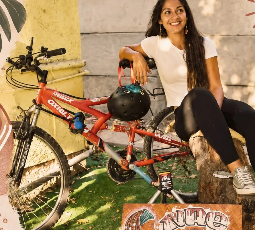 Nae sentada junto a su bicicleta roja y el letrero pintado de su puesto Nae Dreadlocks